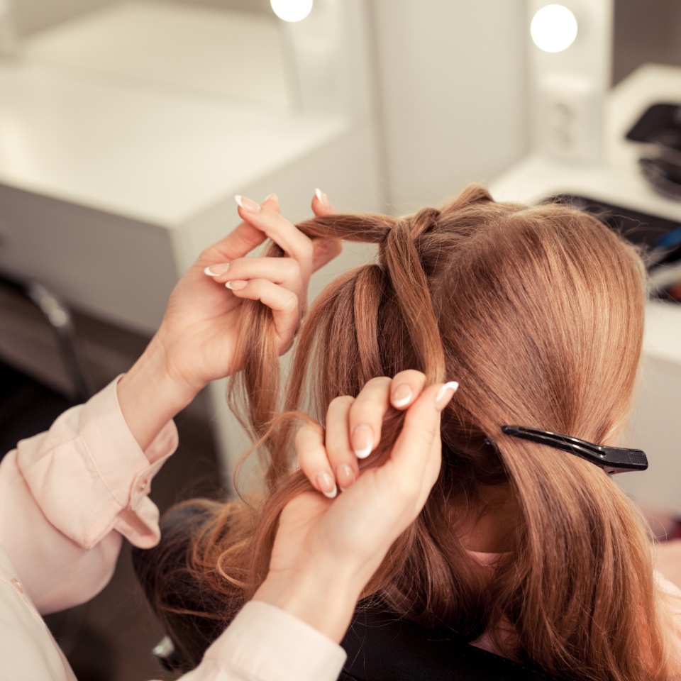 The work of the stylist on hairstyles in a bright salon, the girl makes curls and braids braids of a small beautiful model, indoor