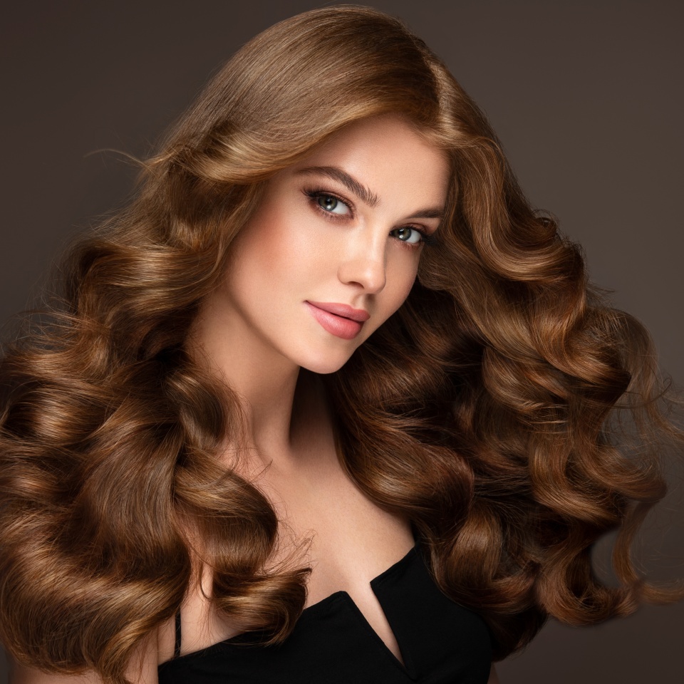Beautiful brunette model girl with long curly hair . Smiling woman hairstyle wavy curls . Fashion , beauty and makeup portrait. Treatment, care and spa procedures.